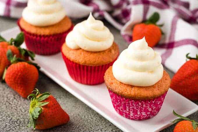 Three strawberry champagne cupcakes in red liners on a plate.