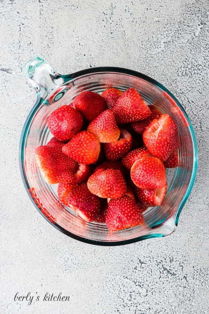 The washed and trimmed strawberries in a glass measuring cup.