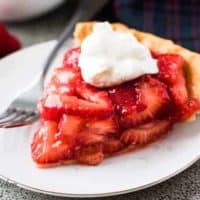 The strawberry pie topped with whipped cream on a plate.