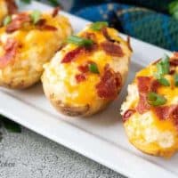 Four twice baked potatoes with cheese on a rectangular platter.