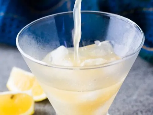 The cocktail being poured into a martini glass with ice.