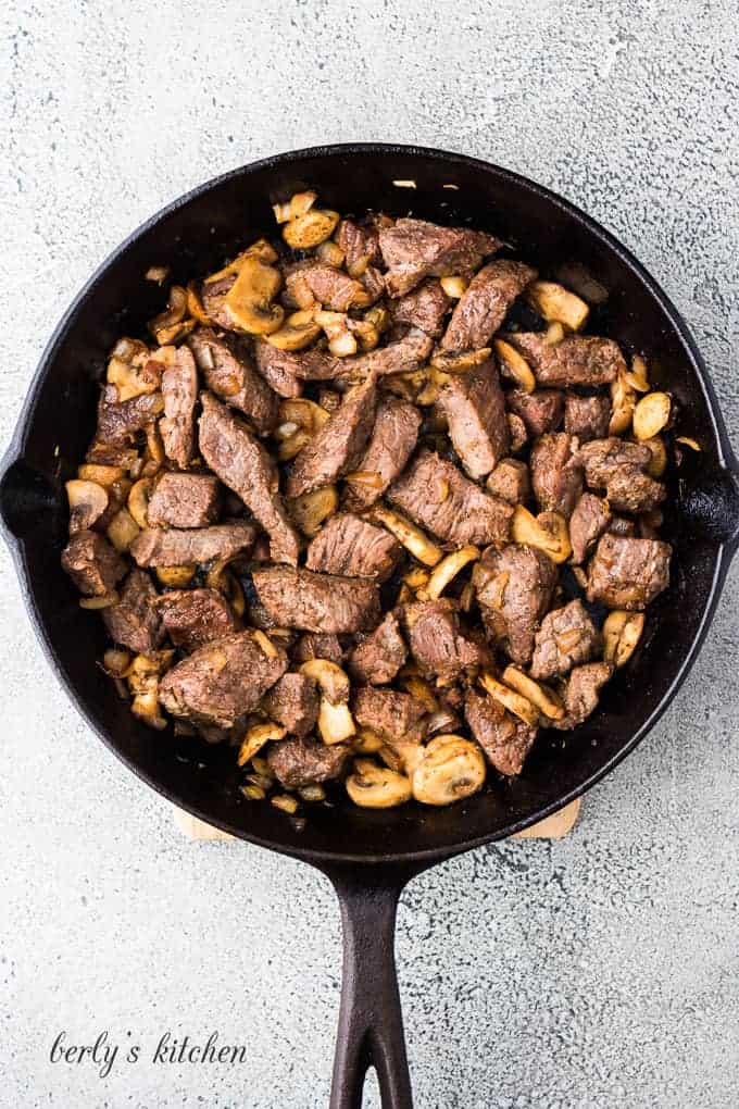 The meat and mushrooms cooking in a skillet with oil.
