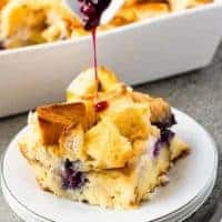 Blueberry sauce being poured over a piece of the casserole.