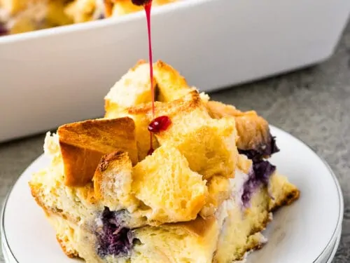 Blueberry sauce being poured over a piece of the casserole.