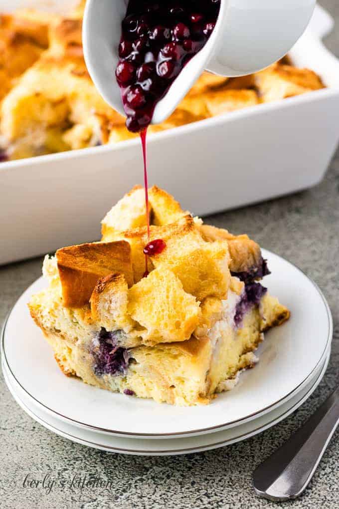 Blueberry sauce being poured over a piece of the casserole.