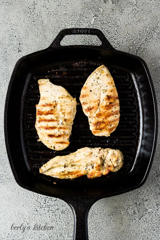 Three chicken breasts cooking in a flat iron griddle pan.