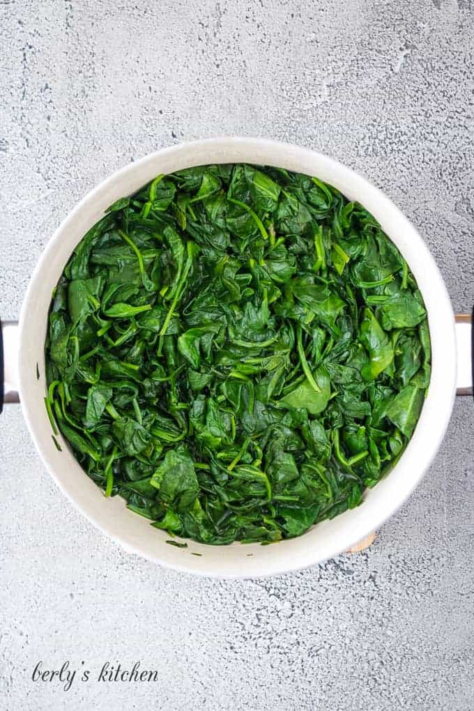 Washed fresh spinach being sauteed in a large metal skillet.