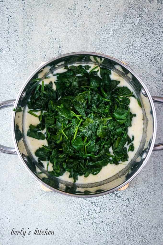 The cooked spinach being added to the bechamel cream sauce.