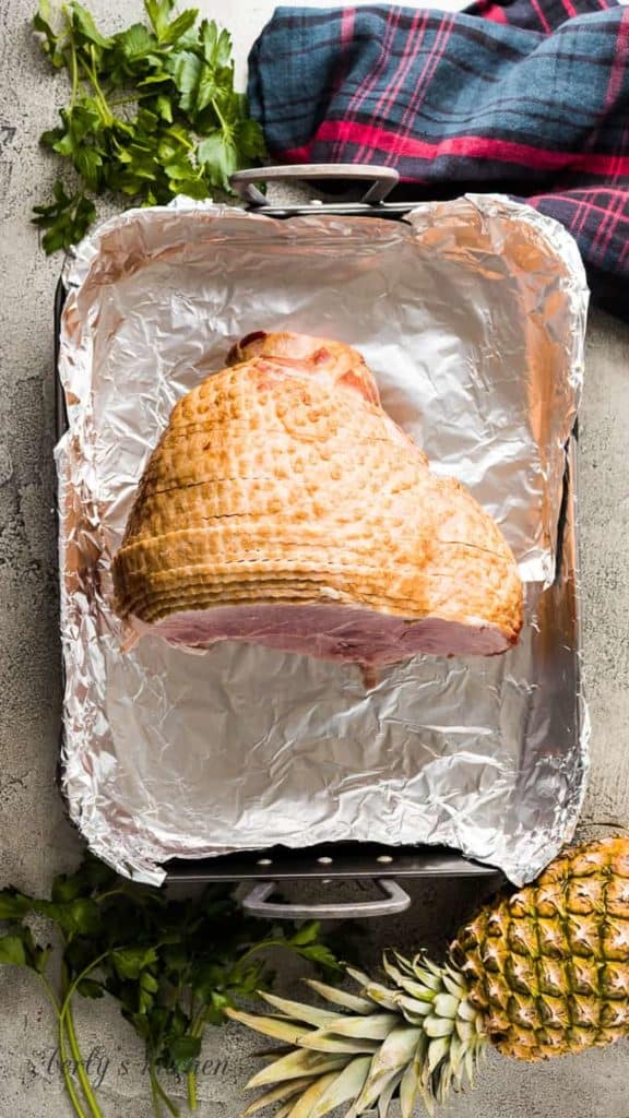 A ham in a roasting pan lined with aluminum foil.