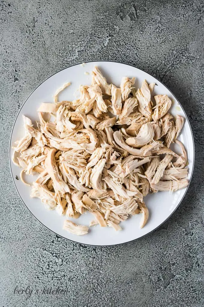 Cooked chicken has been removed and shredded on a plate.