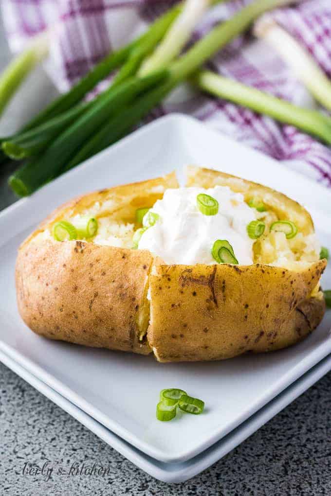 The cooked potato topped with sour cream, butter, and onions.