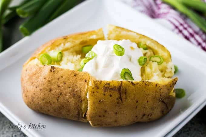 The baked potato on a plate with chives and sour cream.