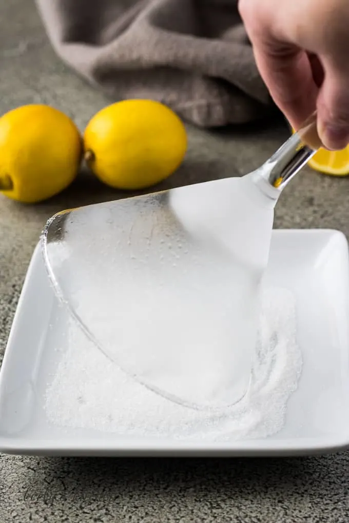 A martini glass being dipped into a dish of sugar.