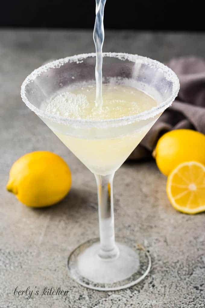 The martini mixture being poured into the chilled martini glass.