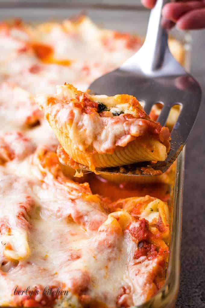 One cheesy pasta shell being lifted from the baking dish.