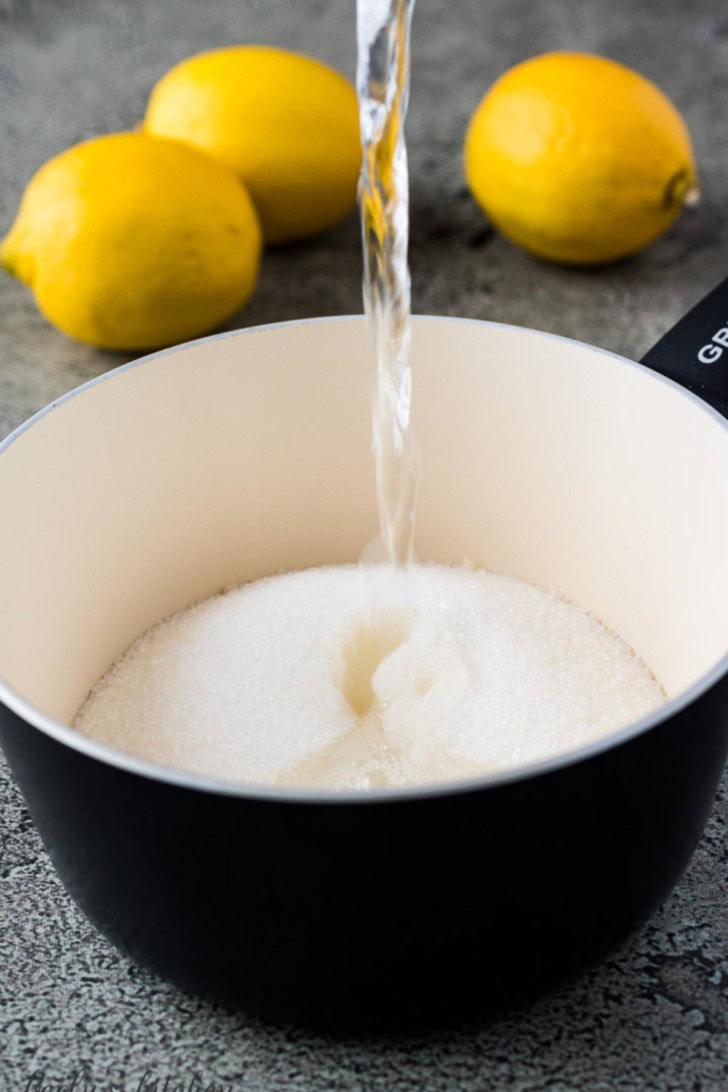 A cup of water pouring into a saucepan with sugar.