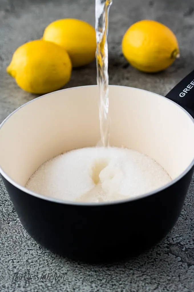 A cup of water pouring into a saucepan with sugar.