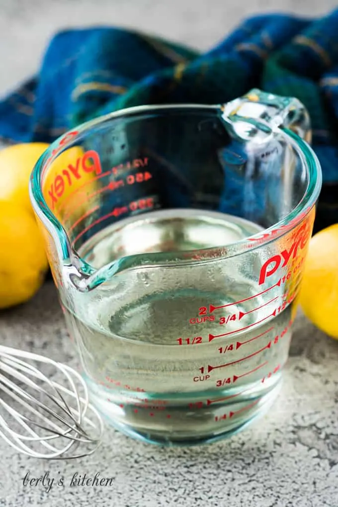 The syrup in a measuring cup surrounded by fresh lemons.