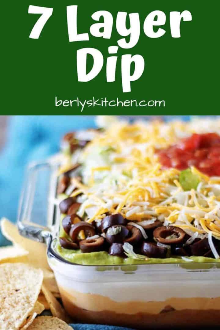 Dish of 7 layer dip sitting on a blue towel with chips.