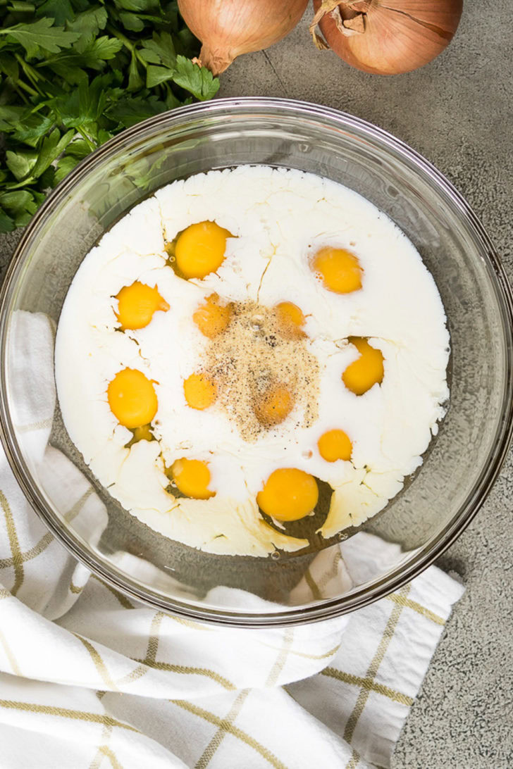Twelve eggs and whole milk in a mixing bowl.