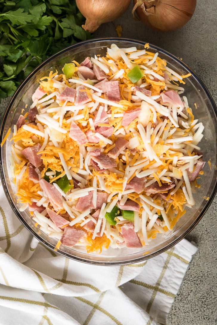 Hash browns, cheese, peppers and other ingredients in a bowl.