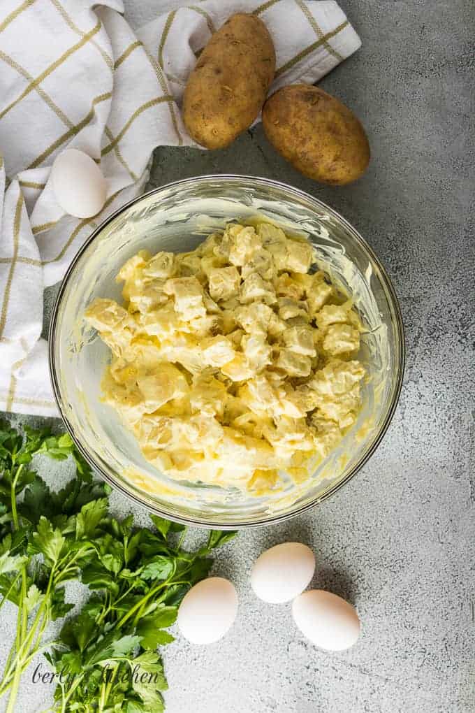 Ariel view of a large bowl of potato salad next to large potatoes and eggs.