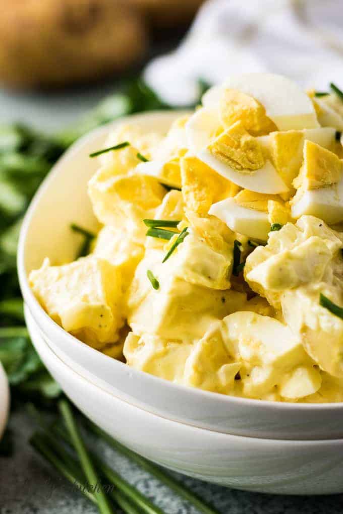 Close up view of potato salad in a white bowl topped with fresh chives.