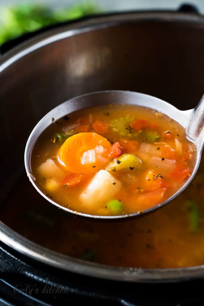 A scoop of the veggie soup in a metal ladle.