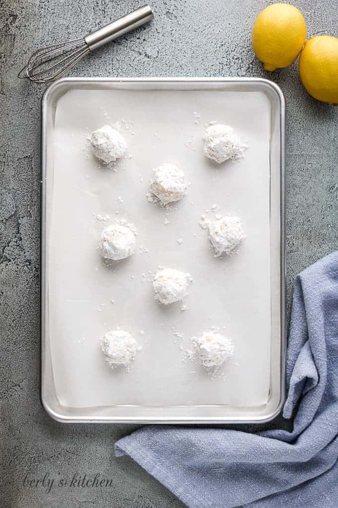 Six balls of dough dipped in powdered sugar and placed on a sheet pan.