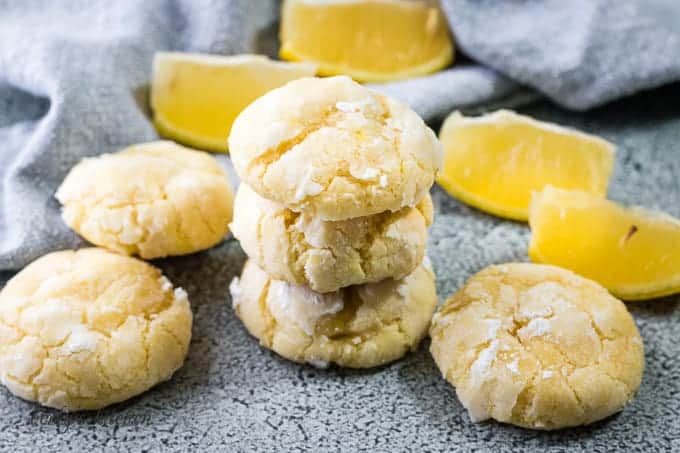 Three stacked lemon crinkle cookies next to fresh lemon slices.