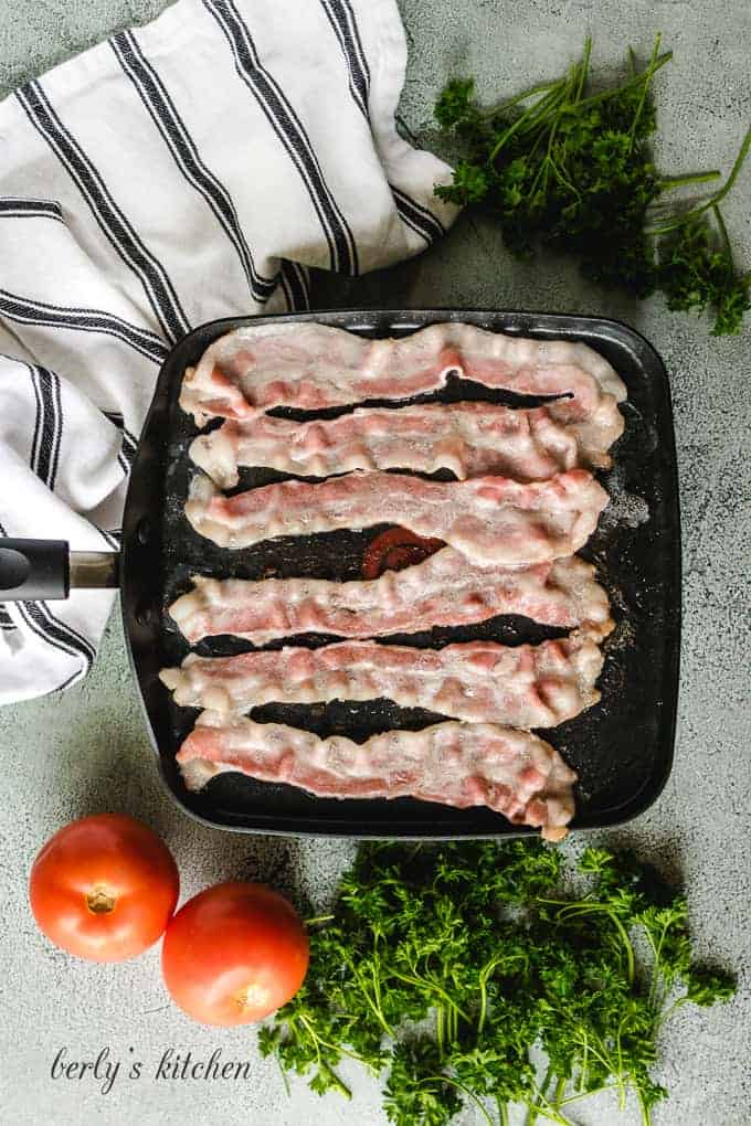 Six pieces of bacon being fried in a large skillet