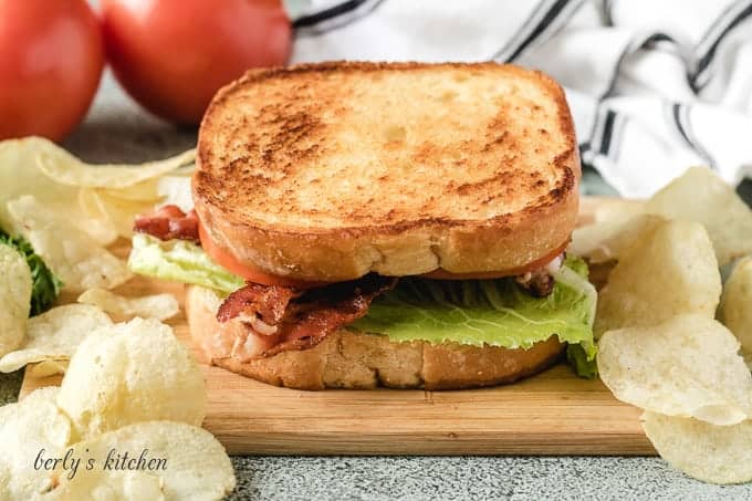 The blt sandwich on a cutting board with potato chips.