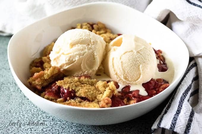 A bowl of cherry dump cake topped with 2 scoops of ice cream.