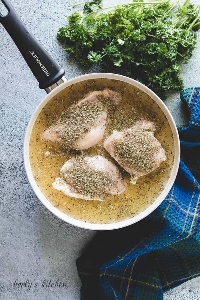 Three seasoned chicken breasts simmering in broth.