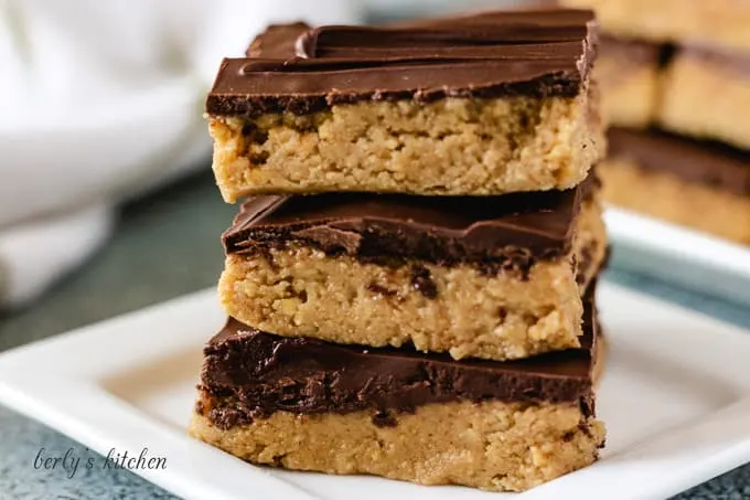 Three chocolate peanut butter bars stacked on a plate.