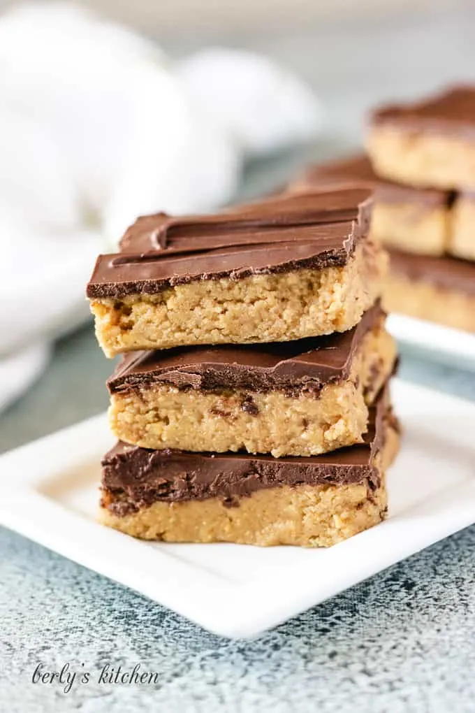 Three no bake chocolate peanut butter bars stacked on a plate.