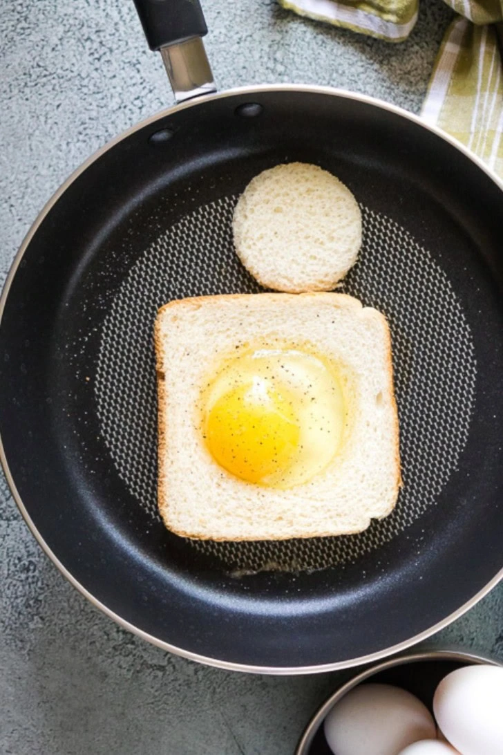 A cracked egg in the center of bread cooking in a skillet.