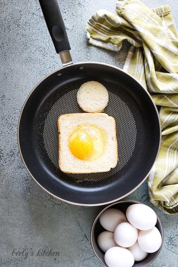 A cracked egg in the center of bread cooking in a skillet.