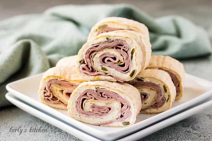 Multiple ham cream cheese pinwheels stacked on a plate.