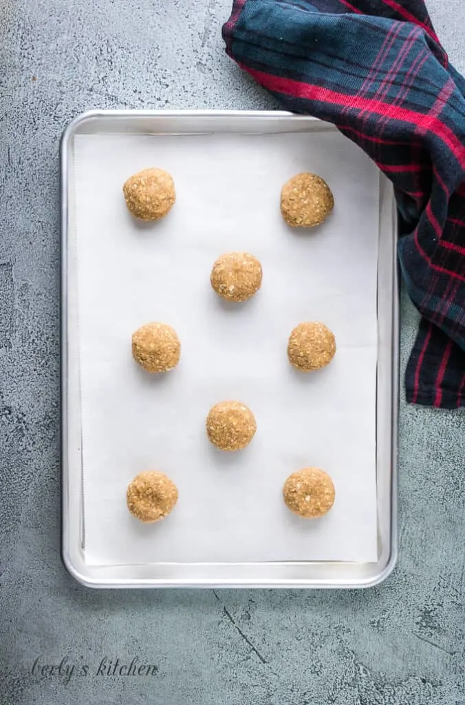 Eight balls of dough on a cookie sheet lined with parchment paper.