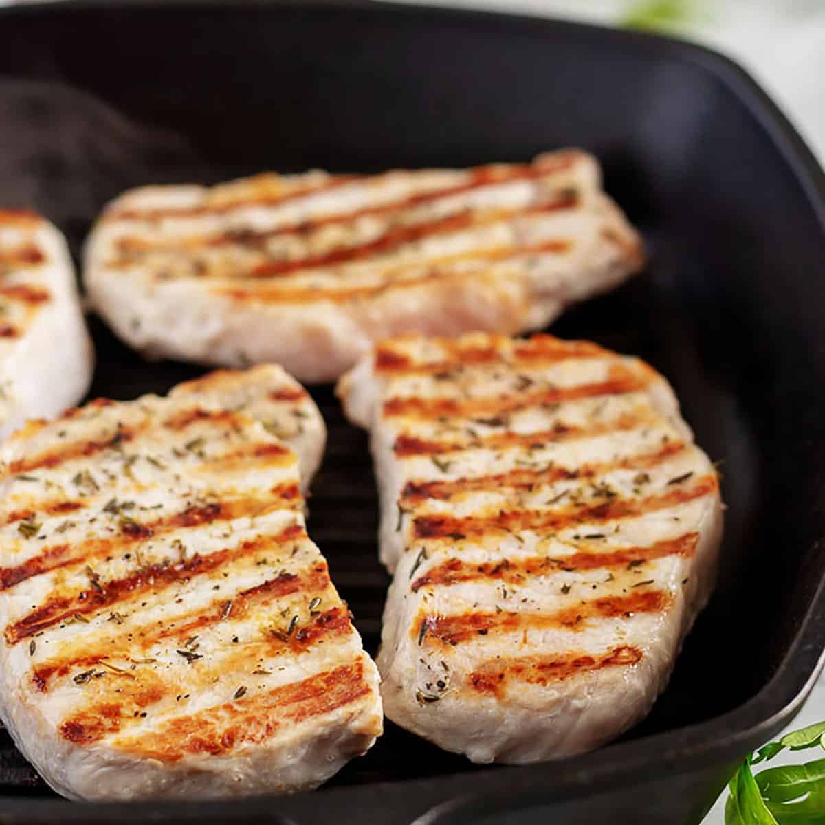 Four grilled pork chops in a cast iron skillet.