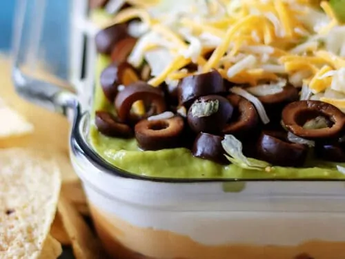 7 layer dip in a dish next to tortilla chips.