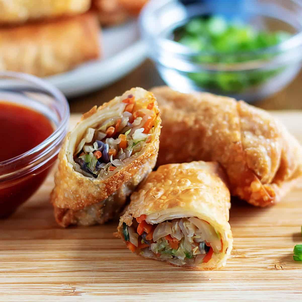 Egg rolls on a cutting board with dipping sauce.
