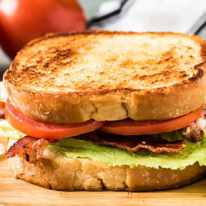 BLT sandwich on a white plate next to mushrooms.