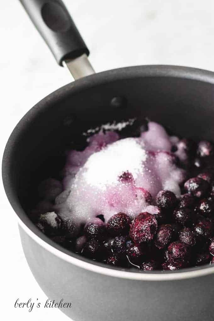 A medium saucepan filled with water, blueberries, and sugar.