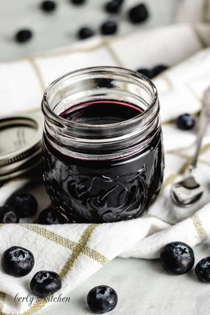 The finished syrup in a jar surrounded by fresh blueberries.