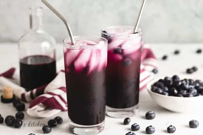 Two glasses of the blueberry soda with metal straws.