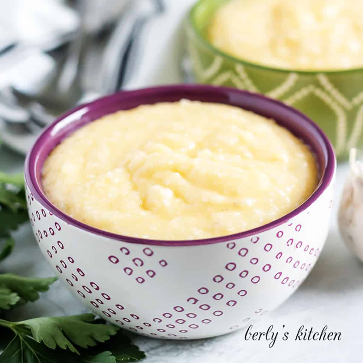 Two bowls of cheese grits next to fresh parsley.