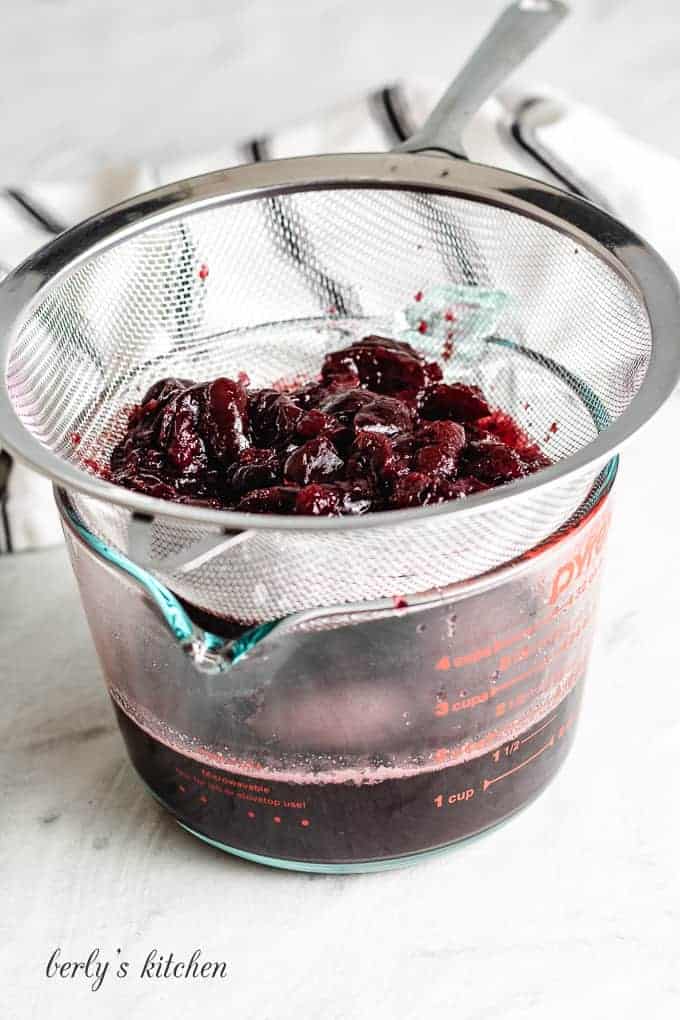 The syrup being strained into a glass measuring cup.