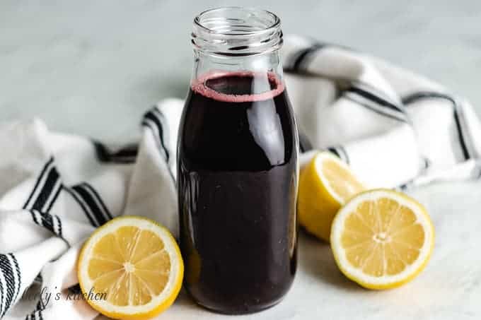 The cherry simple syrup in a bottle surrounded by lemons halves.